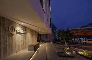 A modern building exterior with a wooden facade, a bench, and a well-lit pathway leading to the entrance. - Alinea Suites Limassol Center (Limassol)