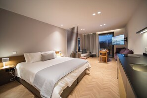 Habitación de hotel moderna con una cama grande, un escritorio, una silla, un sofá y un televisor.