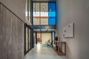 A modern interior with a concrete wall, a wooden bench, a glass door, and a view of a room with a chair and table. - Alinea Suites Limassol Center (Limassol)