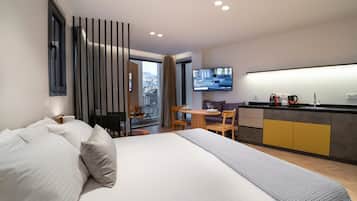 Quarto de hotel moderno com uma cama grande, área de refeições e televisão exibindo uma mensagem de boas-vindas.