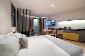 A modern hotel room with a large bed, a dining area, and a TV displaying a welcome message.