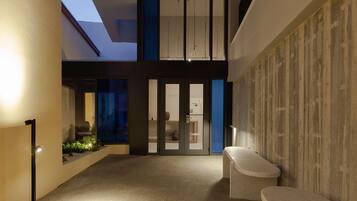 A modern interior with a high ceiling, a seating area, and a view through a glass door.