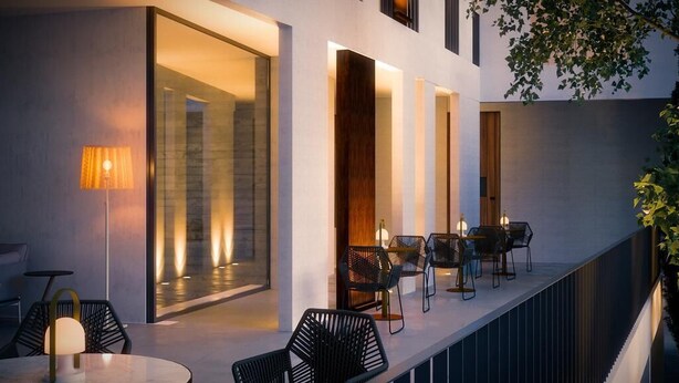 A modern outdoor seating area with tables and chairs, a glass wall, and a wooden door. - Alinea Suites Limassol Center (Limassol)