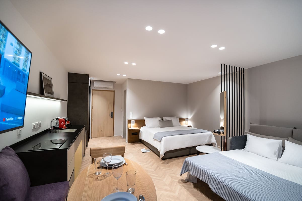 A modern hotel room with a TV, a desk with a coffee machine, a bed, bedside tables, and a sofa.