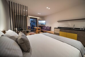 A modern hotel room with a large bed, a desk, a sofa, and a TV. - Alinea Suites Limassol Center (Limassol)