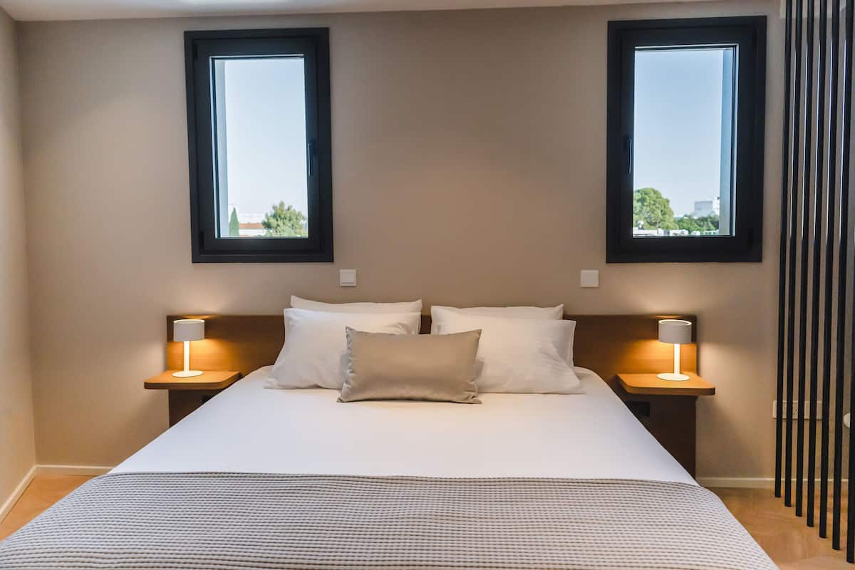 A bedroom with a large bed, two bedside tables with lamps, and two windows.