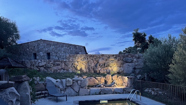 Un bâtiment en pierre doté d’une piscine et de chaises longues.