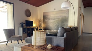 Un salon moderne avec un canapé gris, une table basse en bois, un téléviseur et un grand tableau abstrait accroché au mur.