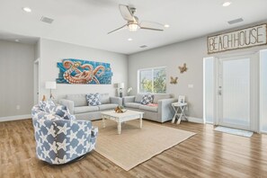 Ein Wohnzimmer mit Deckenventilator, einem Oktopusgemälde und einem Schild mit der Aufschrift 'BEACHHOUSE'.