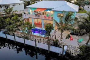 Ein zweigeschossiges Haus mit Balkon, Schwimmbad und Steg, der sich ins Wasser erstreckt.