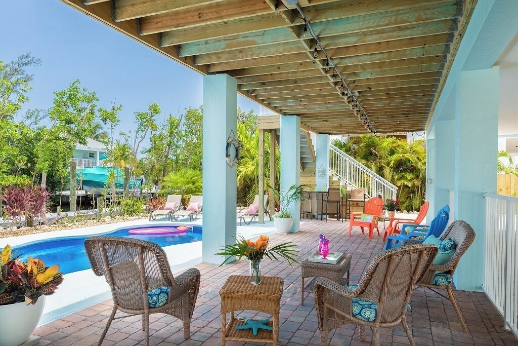 A covered outdoor area with a pool, wicker furniture, and a staircase leading to a higher level.