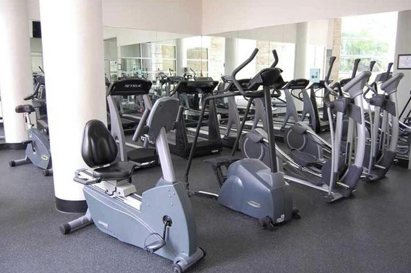 A gym with multiple exercise machines, including treadmills and elliptical trainers, arranged in rows.