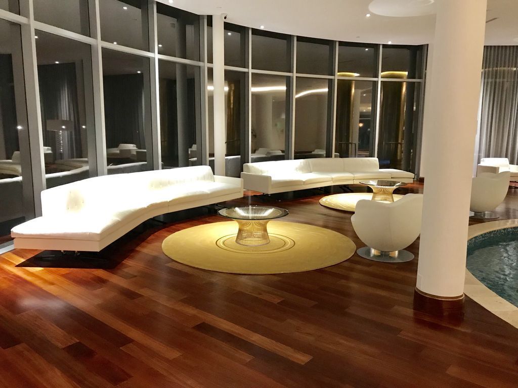 Un interior moderno con un sofá blanco curvo, una mesa de centro redonda de vidrio y una piscina visible a través de amplios ventanales.