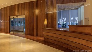 A modern lobby with wooden paneling, a reception desk, and a large window with a view of palm trees.