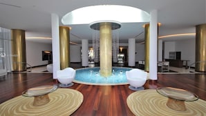 A modern lobby with a central water feature, white chairs, and a circular seating area.