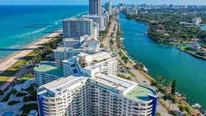 A high-rise hotel with multiple balconies, a swimming pool, and a view of the ocean and city skyline.