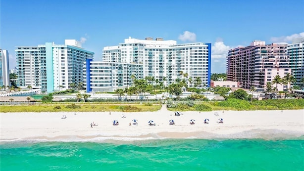 A beachfront hotel with multiple high-rise buildings, a sandy beach, and clear turquoise waters.