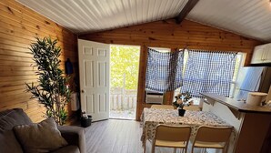 Interior acollidor d'una cabana amb sòl de fusta, un sofà, una taula de menjador amb cadires i una zona de cuina.