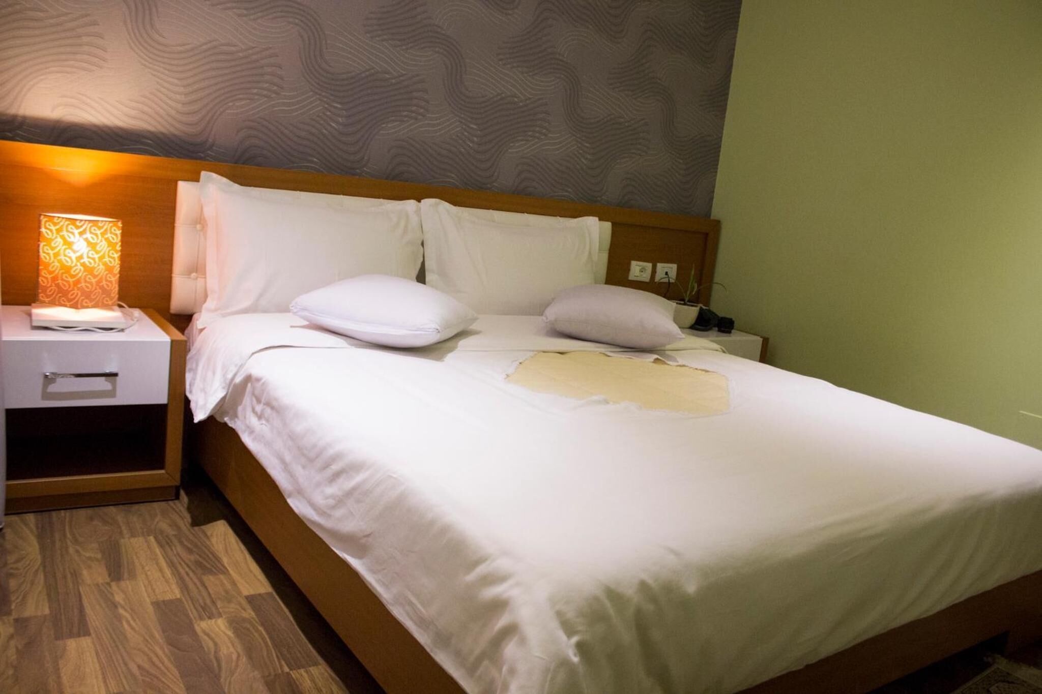 Una cama bien hecha con sábanas y almohadas blancas, una lámpara de noche y un cabecero de madera.