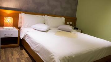 Una cama bien hecha con sábanas y almohadas blancas, una lámpara de noche y un cabecero de madera.