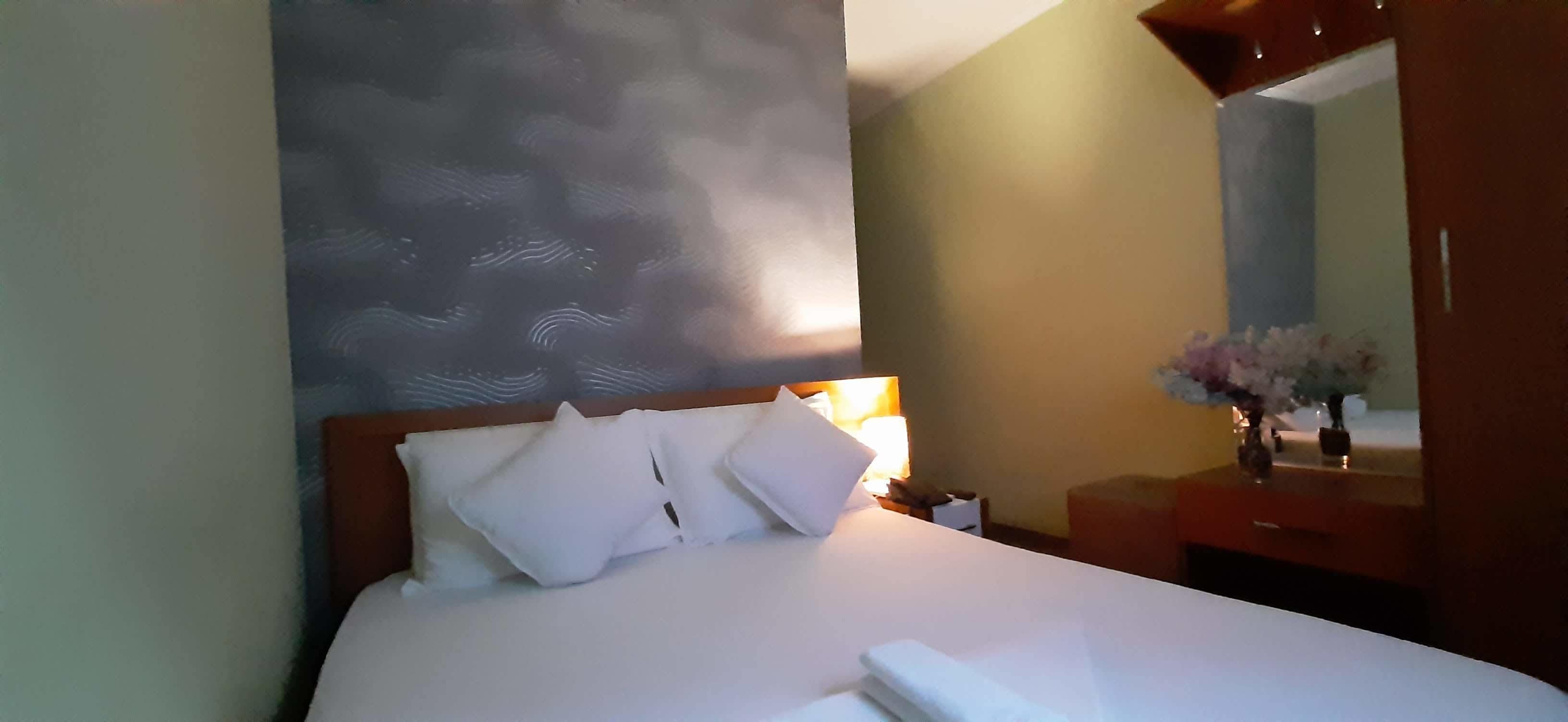 A hotel room with a bed, a nightstand, a mirror, and a vase with flowers.