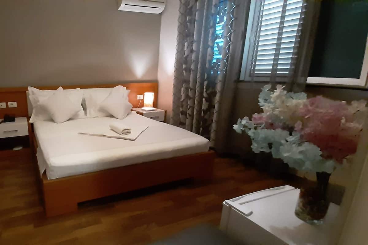 Ein Hotelzimmer mit einem hölzernen Bett, weißen Leinentüchern, einem Nachttisch mit Lampe und einer Blumenvase.