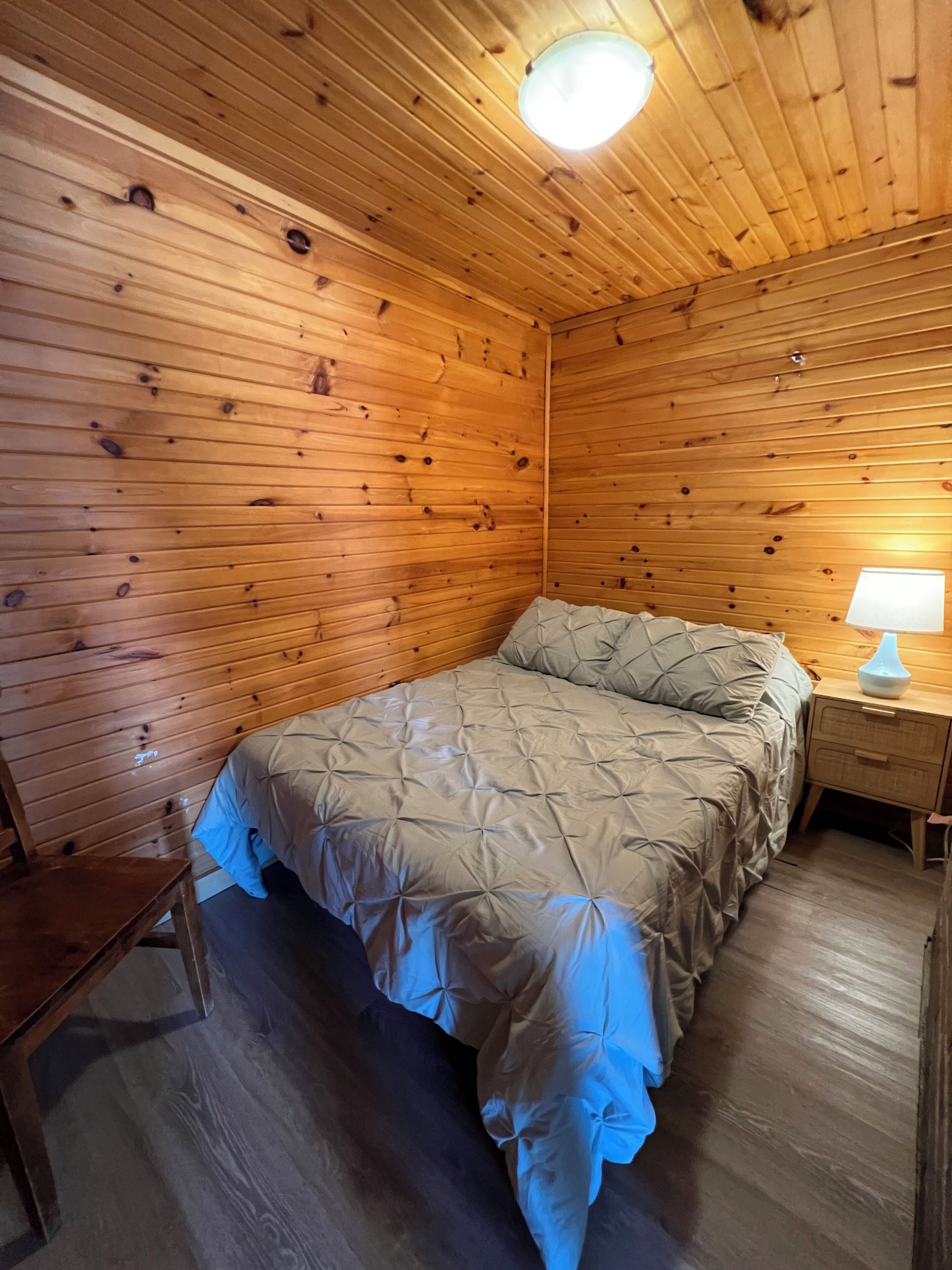 Una habitación con paneles de madera, una cama, una mesita de noche y una silla.