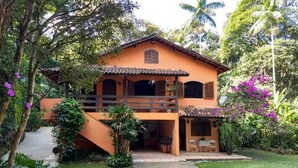 A two-story house with a balcony, surrounded by lush greenery and flowering plants. - HOUSE IN PENEDO WITH WATERFALL (Penedo)