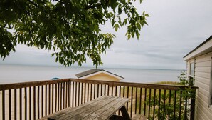 A wooden deck with a picnic table, overlooking a beach and a body of water. - BEACHFRONT COTTAGE IN WASAGA BEACH - SANDPIPER BEACH RESORT - COTTAGE # 9 (Wasaga Beach)