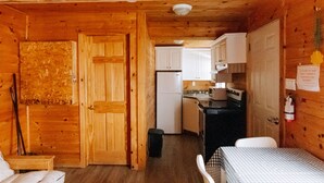A wooden cabin interior with a kitchen, a dining area, and a small bedroom. - BEACHFRONT COTTAGE IN WASAGA BEACH - SANDPIPER BEACH RESORT - COTTAGE # 9 (Wasaga Beach)
