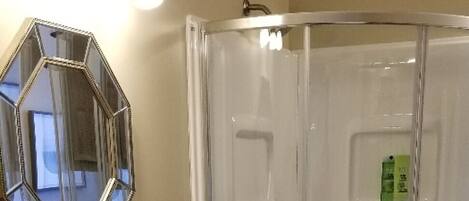 Un baño con lavamanos blanco, espejo, ducha y toallero.