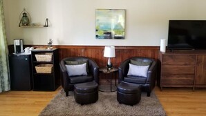 Una sala de estar con dos sillones de cuero, una estación de café, un televisor de pantalla plana y un mueble de madera.