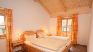Una cama con estructura de madera y ropa de cama blanca en una habitación con piso de madera y techo inclinado.