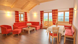 Una sala de estar acogedora con techo de madera, muebles rojos y ventanas amplias que dan al exterior.