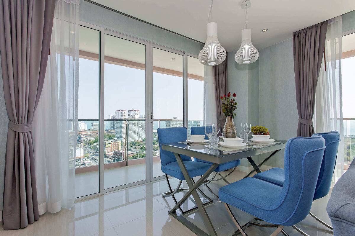 Ein moderner Essbereich mit einem Glastisch, blauen Stühlen und Blick auf die Stadt durch große Fenster.