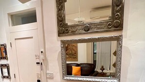 Un comedor con una mesa de madera y sillas verdes, un espejo grande con un marco ornamentado, y una puerta con un pequeño ventanal.