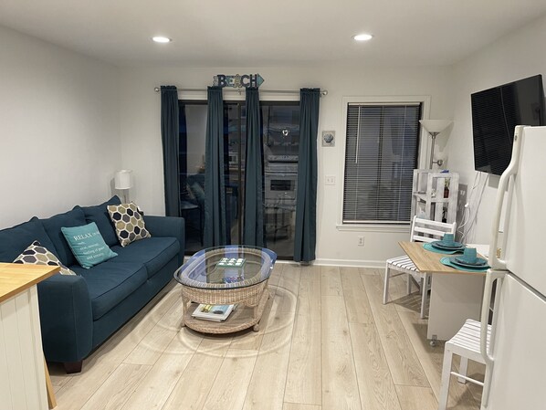 A modern living room with a blue sofa, a glass coffee table, and a dining area with a white table and chairs.