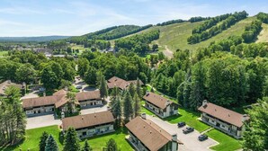 A residential area with multiple two-story houses, surrounded by lush greenery and hills in the background. - Boyne Mountain, Base of Mtn, Sleeps 13 (Boyne Falls)