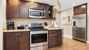 A modern kitchen with dark wood cabinets, stainless steel appliances, and a granite countertop. - Boyne Mountain, Base of Mtn, Sleeps 13 (Boyne Falls)