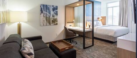 Una habitación de hotel moderna con sofá, escritorio, cama y una ventana grande.