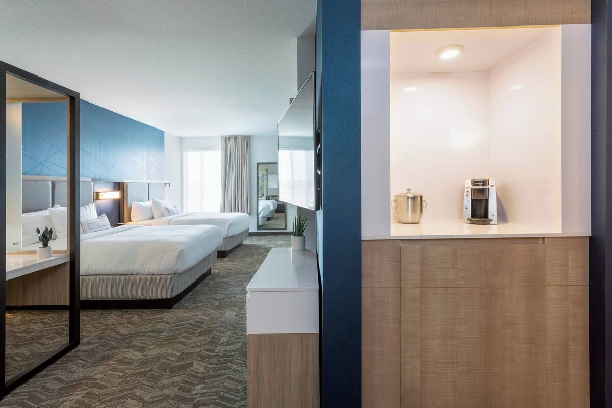 A hotel room with a large bed, a smaller bed, a desk, and a coffee machine.
