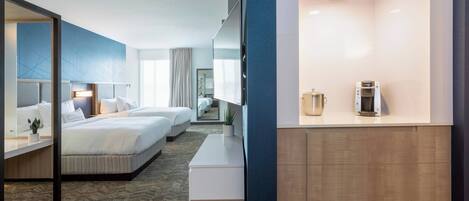 Una habitación de hotel con una cama grande, una cama más pequeña, un escritorio y una cafetera.