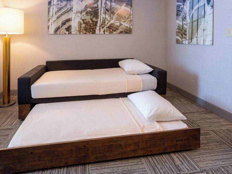 Cama doble con estructura y cabecera de madera, lámpara de noche y cuadro abstracto en la pared.