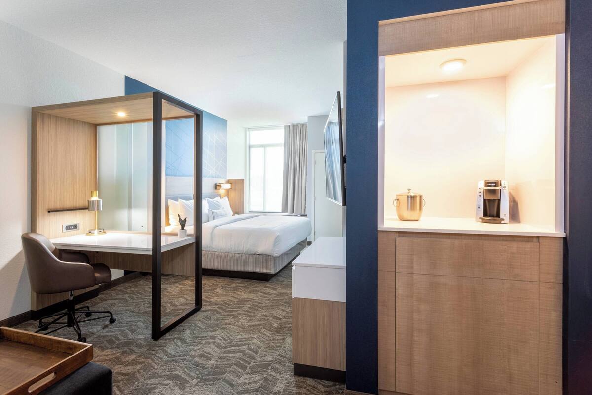 A hotel room with a desk, a bed, a shower area, and a kitchenette.