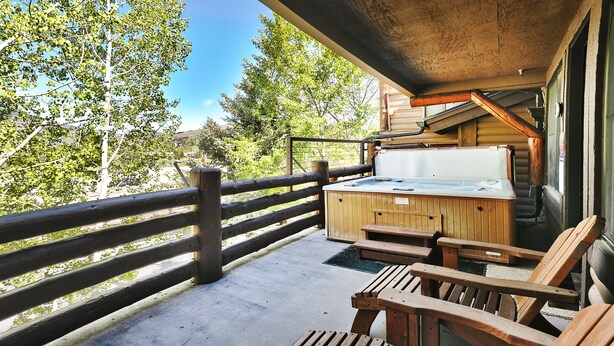 Una terraza de madera con un jacuzzi, sillas de madera y una mesa de madera.