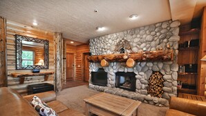Interior de una cabaña de troncos con chimenea de piedra, sofás de cuero y una mesa de centro de madera.