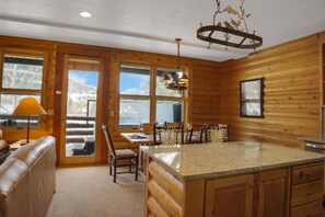 A log cabin interior with a kitchen area featuring a granite island, wooden dining table, and chairs.