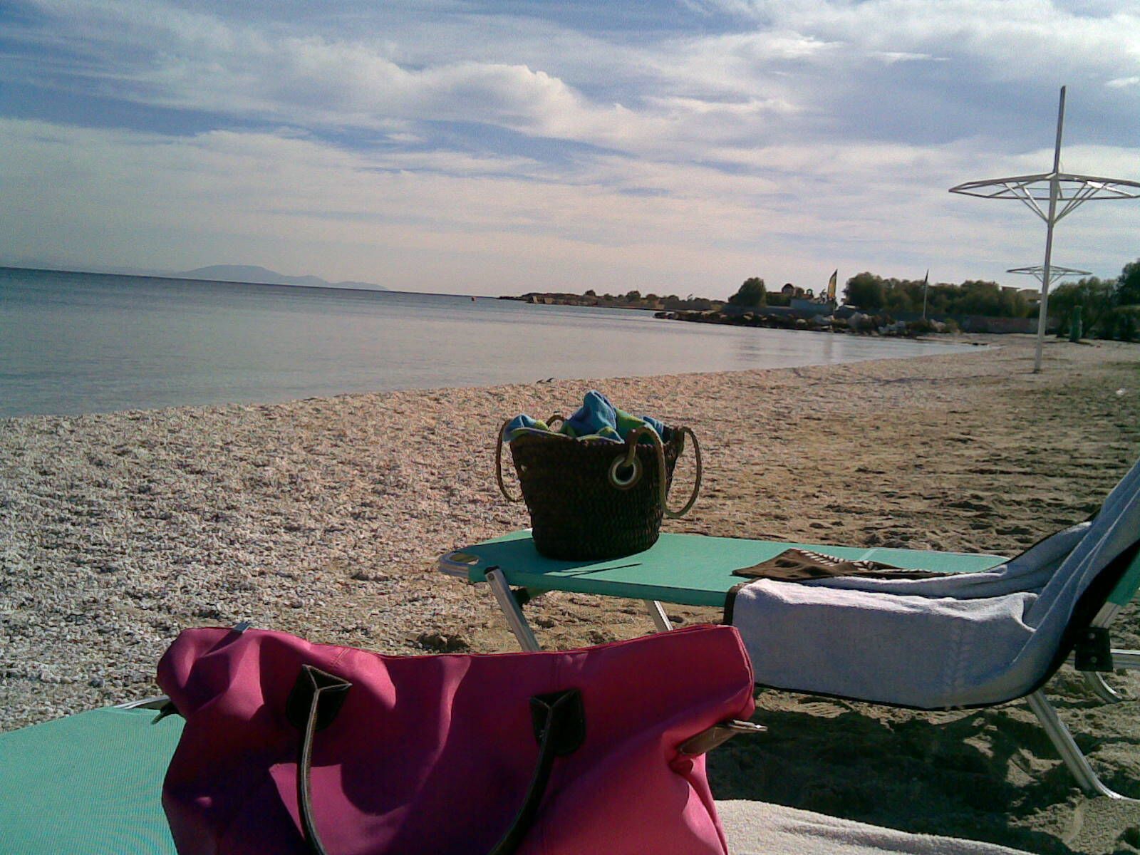 A beach with a chair and a bag on the sand, a small table, and a distant umbrella structure.
