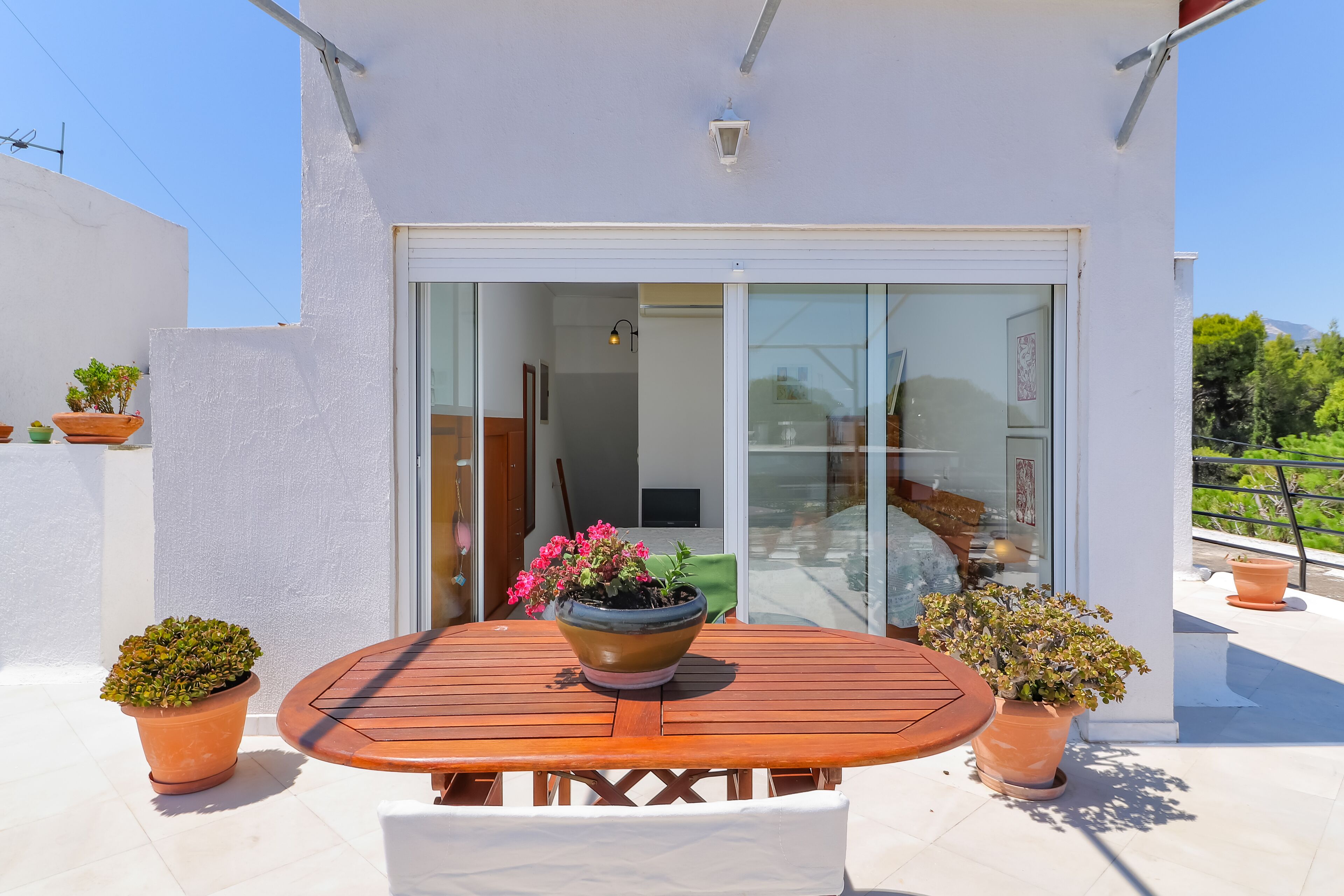 A patio with a wooden table and chairs, surrounded by terracotta pots with plants.