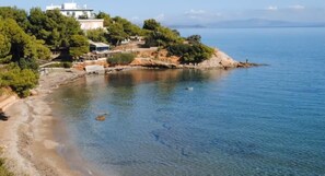 Une propriété située sur la côte, avec une plage, un bâtiment à la façade blanche et une vue dégagée sur la mer.